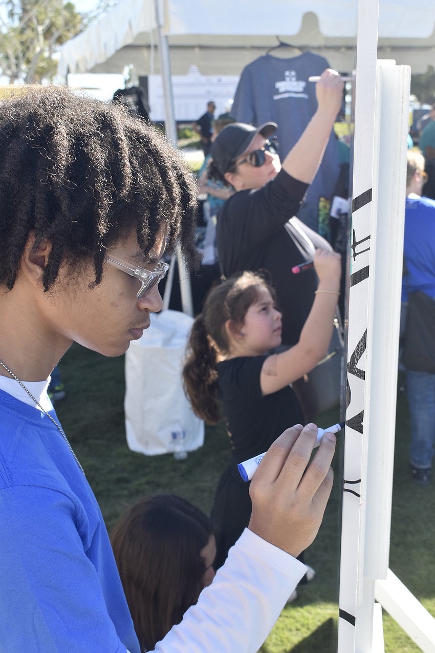 Jaden Stotz, 16, adds to a piece of community artwork alongside Piper Borgia-Howard, 7, and Kelly Borgia of Gulf Coast Community Foundation.