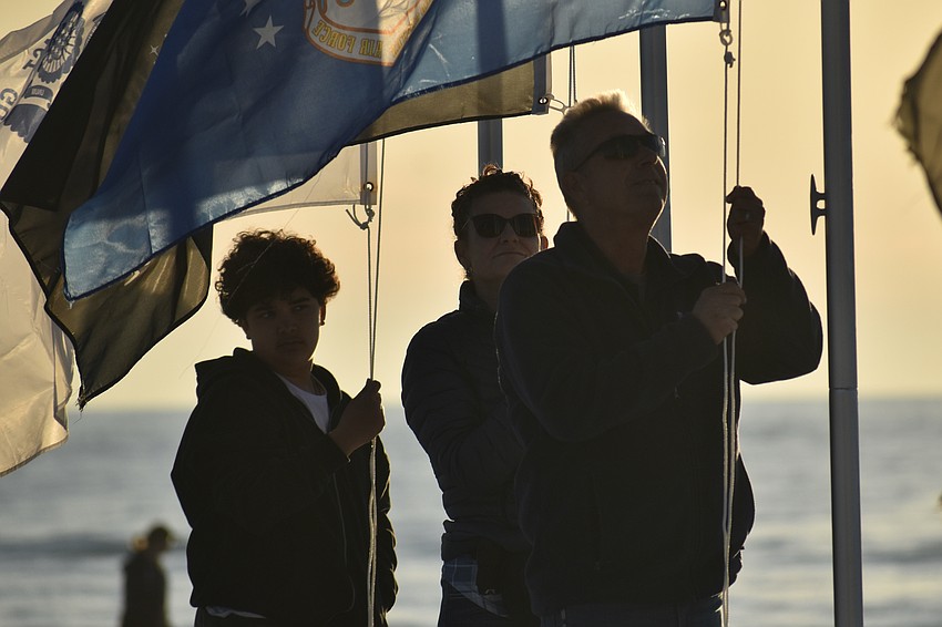 Blayton Bidlestone, 13, raises the flag of the Coast Guard, standing beside Vanessa Lima, who raised the Space Force flag, and James 