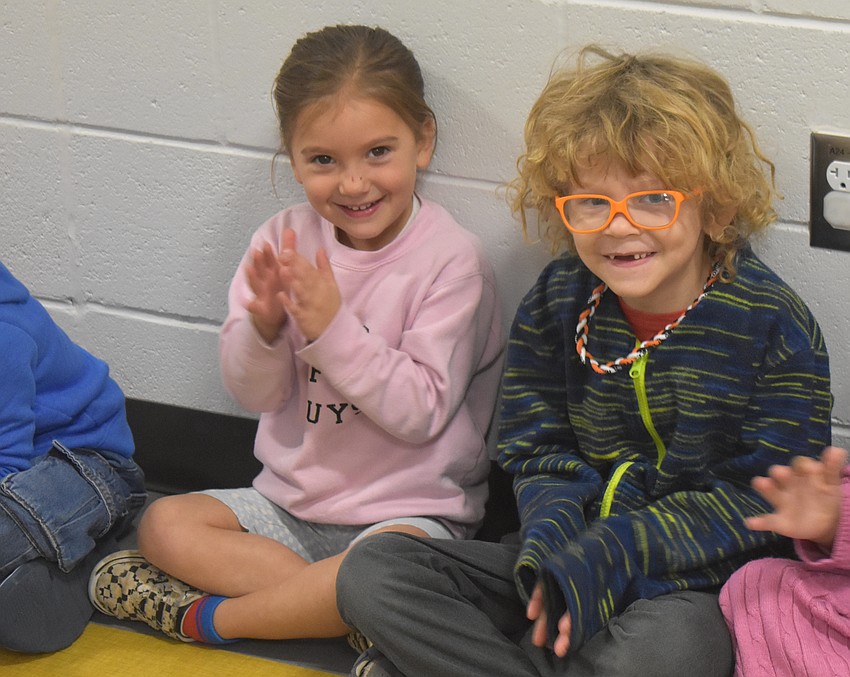 Harlyn Cuviello and Ellis Krogh, pre-k students at Tara Elementary, watch as older students walk through the halls in bright colors holding flags.