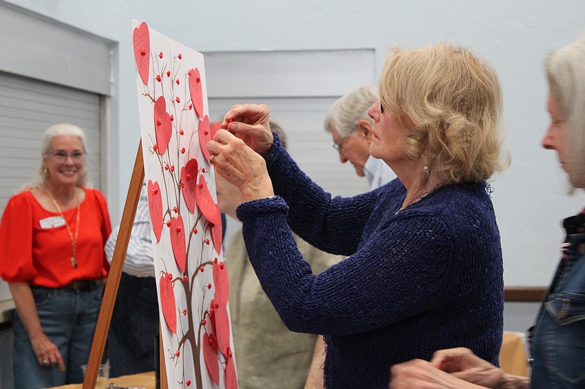 Mary Jane Tolpa affixes a prayer intention to the heart tree on display at the Women's Guild Valentine's Day art show.