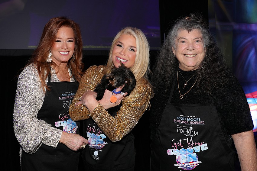 Terri Klauber hands over the yet unnamed Yorkie pup to auction winner Elizabeth Giuliani. Christine Merkent is the breeder and donated the pup from Minimagic Yorkshire Terriers to Cooking for Wishes.