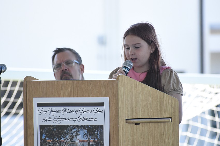 Principal Chad Erickson stands beside fourth grader Lorelei Martin as she reads her essay.