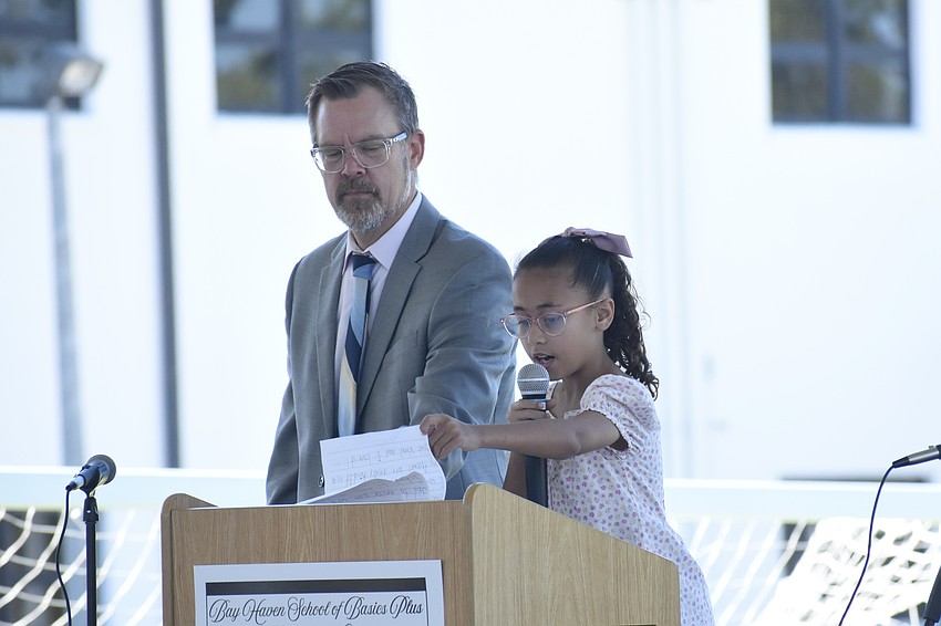 Principal Chad Erickson stands beside first grader Jade Rivers as she reads her essay.