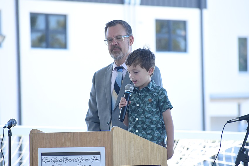 Principal Chad Erickson stands beside kindergartener Logan Hernandez as he reads his essay.