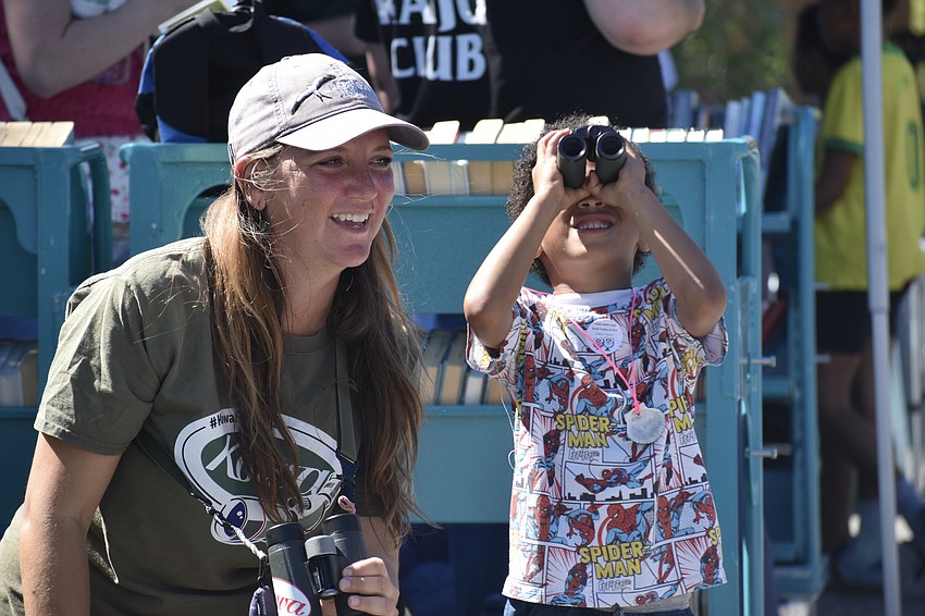 Mariah Hryniewich of Kowa Sporting Optics helps Elijah Adamo, 4, as he tries out a pair of binoculars.