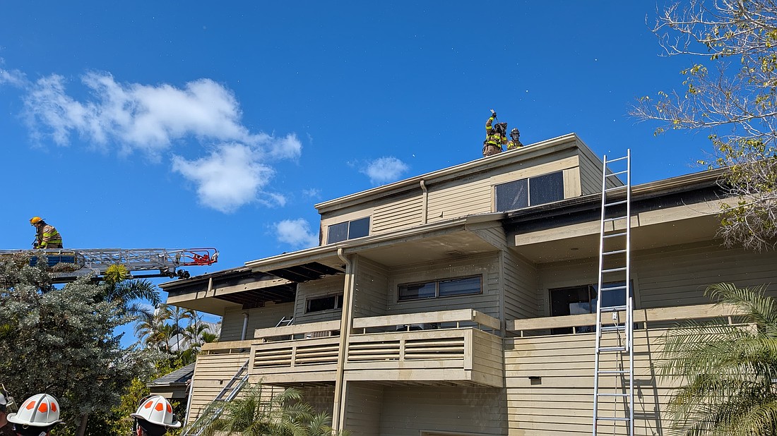 Firefighters break a hole in the roof of a building minutes after first responders extinguished the flames that engulfed a three-story residence devastated by what is reported as a potential electrical fire Monday, Feb. 23.