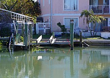 A boat is attached by a red strap to land as it lies under a dock in disrepair in a canal off General Harris Street. Longboat Key Fire Department determined the vessel is not leaking fuel.