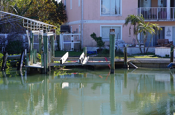 A boat is attached by a red strap to land as it lies under a dock in disrepair in a canal off General Harris Street. Longboat Key Fire Department determined the vessel is not leaking fuel.