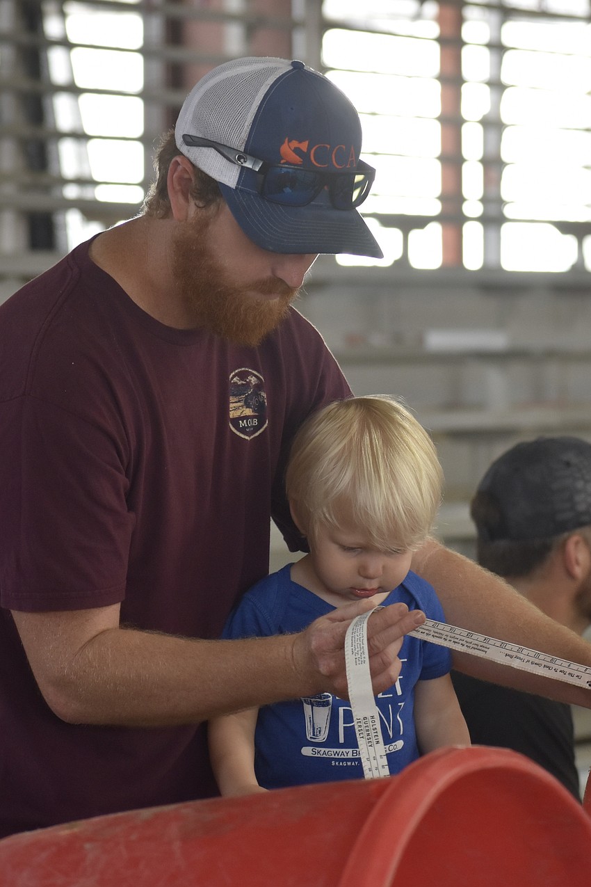 Devin Payne, whose wife Tristian Payne is part of the event's livestock committee, gives their son Ty Payne, 2, a chance to measure an animal, following an activity that simulated different skills.