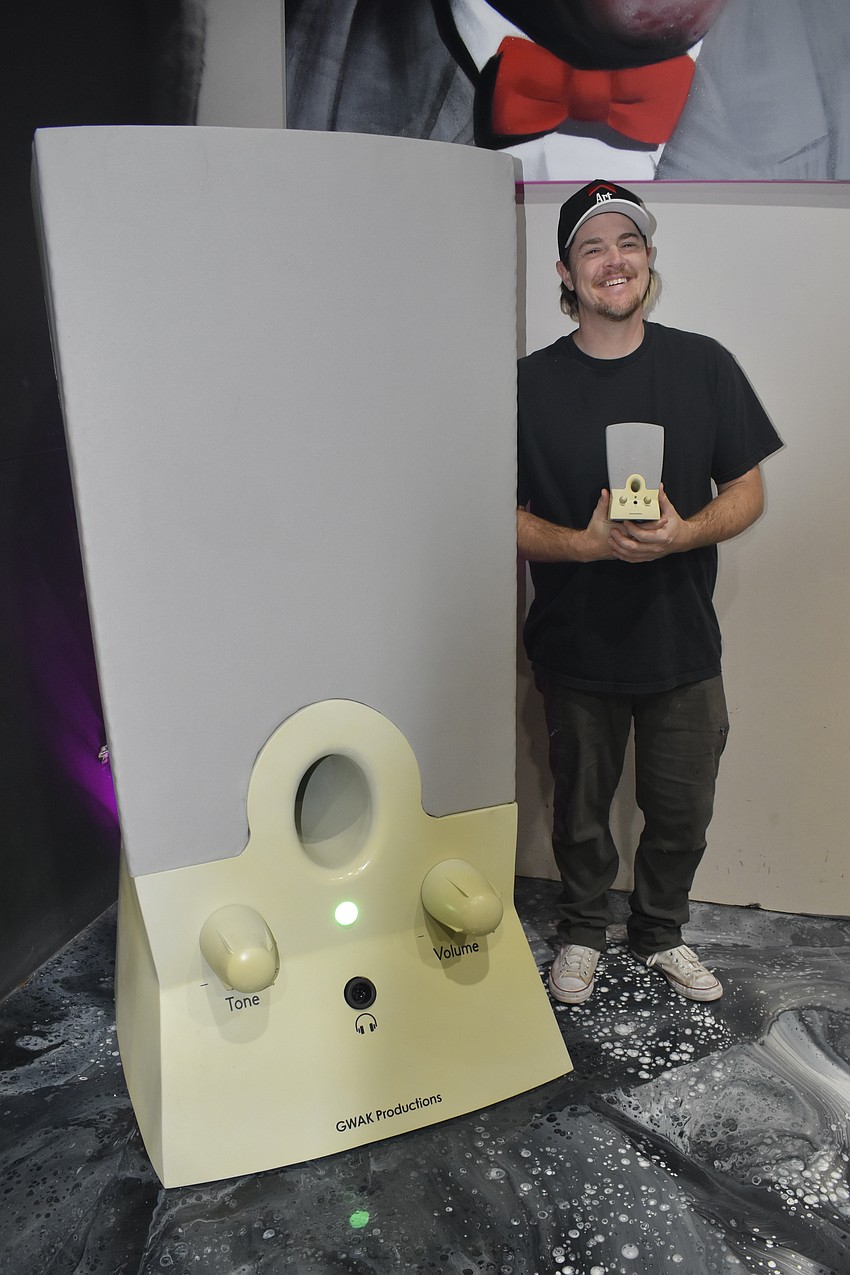 Joel Benham holds a real early 2000's computer speaker as he stands beside his giant functional replica.