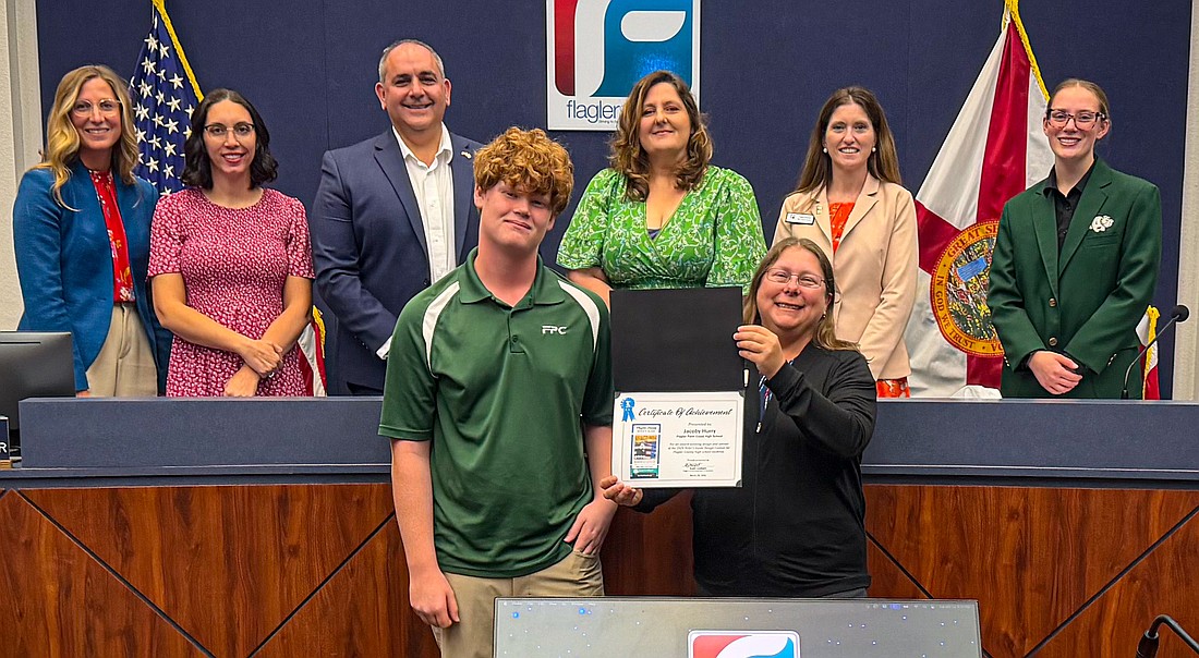 At the March 24 Flagler County School Board meeting, Elections Supervisor Kaiti Lenhart presents Flagler Palm Coast student Jacoby Hurry with a certificate as the winner of the 2026 Flagler County Voter's Guide cover design contest. Courtesy photo, Flagler Schools