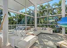 The spacious living area features 16-foot-high ceilings and views out to a forest of palm trees.