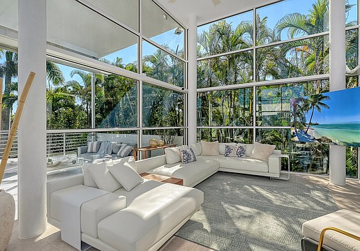 The spacious living area features 16-foot-high ceilings and views out to a forest of palm trees.