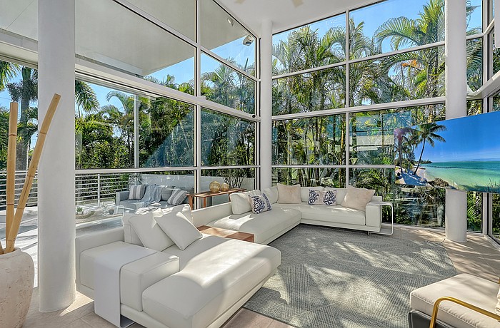 The spacious living area features 16-foot-high ceilings and views out to a forest of palm trees.