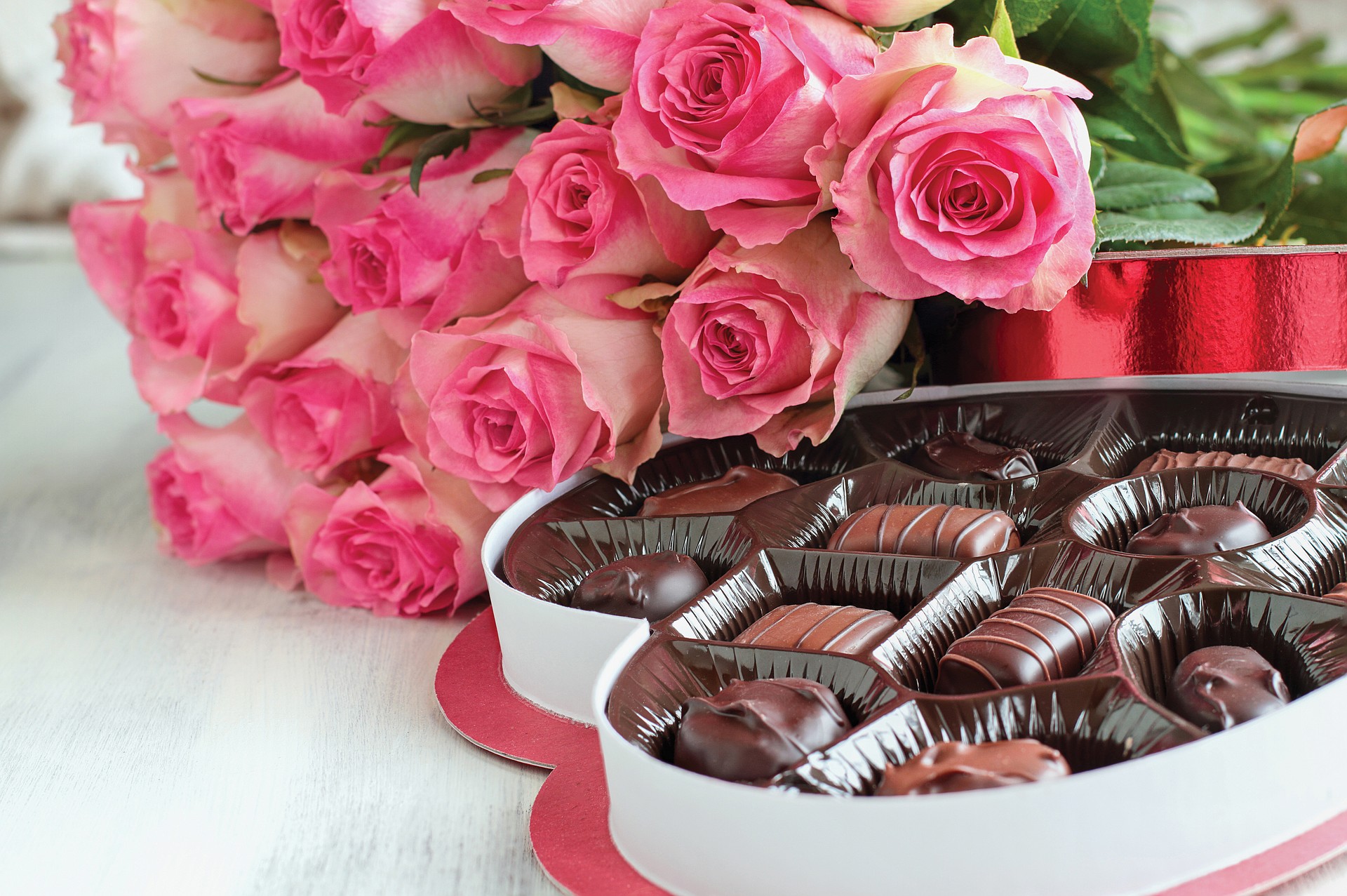 Dozen soft pink rose flowers with a heart shaped box of chocolate candy for Valentine Day over a wood background.