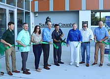 From left, Assistant County Administrator Brad Johnson, County Administrator Jonathan Lewis and County Commissioners Teresa Mast, Ron Cutsinger, Mark Smith, Joe Neunder and Tom Knight flank Matt Osterhoudt as he cuts the ribbon at the new development services one stop shop.