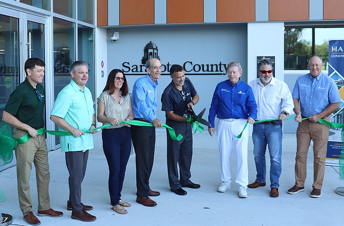 From left, Assistant County Administrator Brad Johnson, County Administrator Jonathan Lewis and County Commissioners Teresa Mast, Ron Cutsinger, Mark Smith, Joe Neunder and Tom Knight flank Matt Osterhoudt as he cuts the ribbon at the new development services one stop shop.