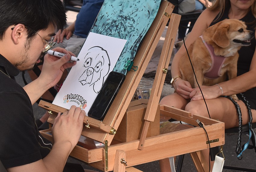 Kelvin Nguyen of Tampa Caricatures draws Kona, a 9-year-old Peagle, at Woofstock on Lakewood Main Street.