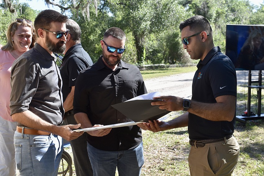 Commission Chair Tal Siddique (on the right) presents Nicholas and Kiel Felts with a sign and proclamation that dedicate the preserve at Crane Park to their late mother Carol Ann Felts.