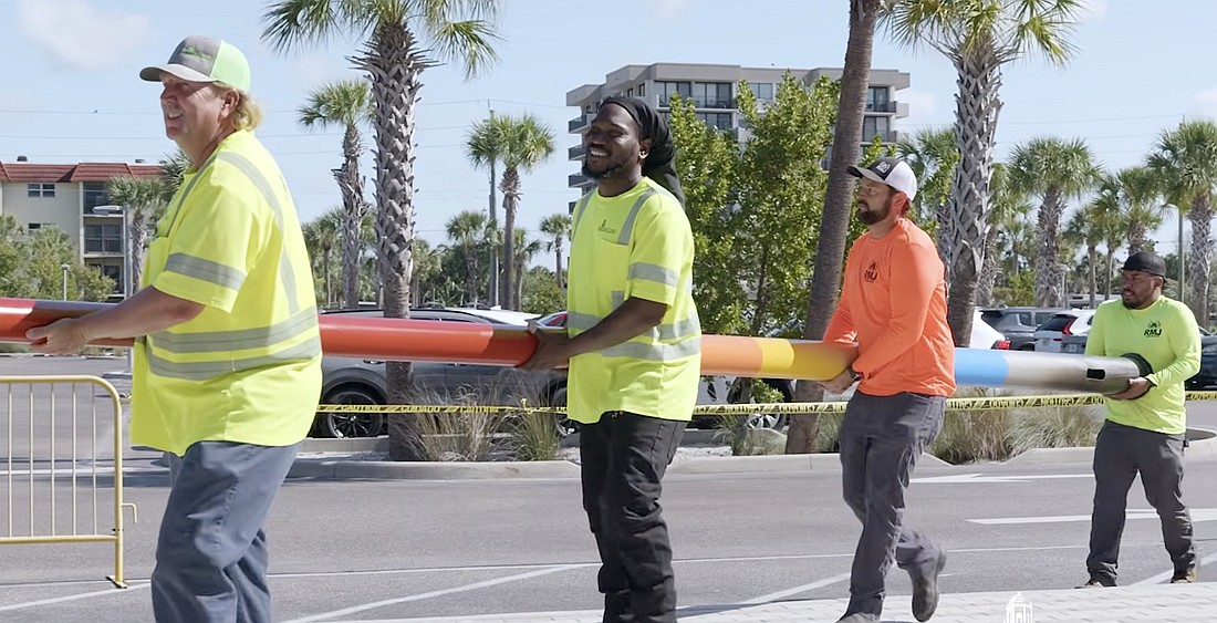 Workers carry one of two storm surge poles Sarasota County has installed at Siesta Beach and Manasota Beach.