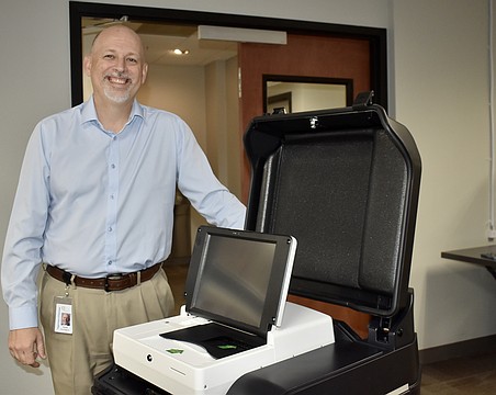 Supervisor of Elections Scott Farrington stands next to one of the new voting machines.