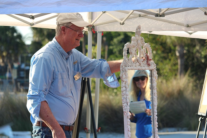 With event organizer Susan Phillips smiling in the reflection, Steve Branham holds up a custom mirror being auctioned at Dinner and a Movie.