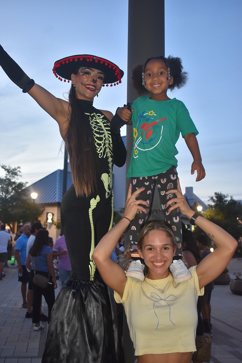Natasha Erickson, a stilt walker with Prism Artistry, is joined by Parrish's Olivia Laws, 5, and Miya Yawn at the Agave Bandido Cinco de Mayo celebration.
