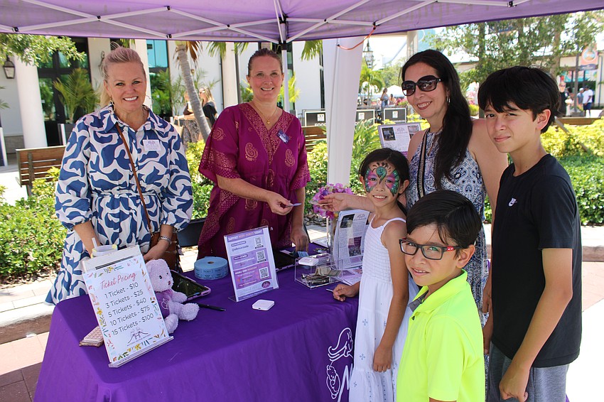 Cheri DeVries and Amanda Hale of Mothers Helping Mothers sell a raffle ticket to Bradenton's Mabel Gomez, who brought her kids, Luca, Jeyden, and Phoenix to Petals and Poses.