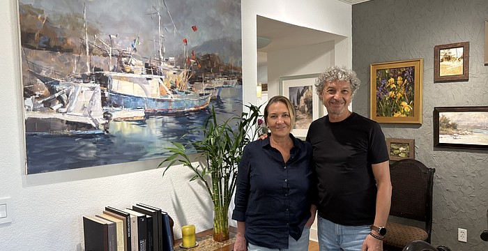 Marina and Vladislav Yeliseyev pose in front of one of Vlad's paintings in their home in The Landings.