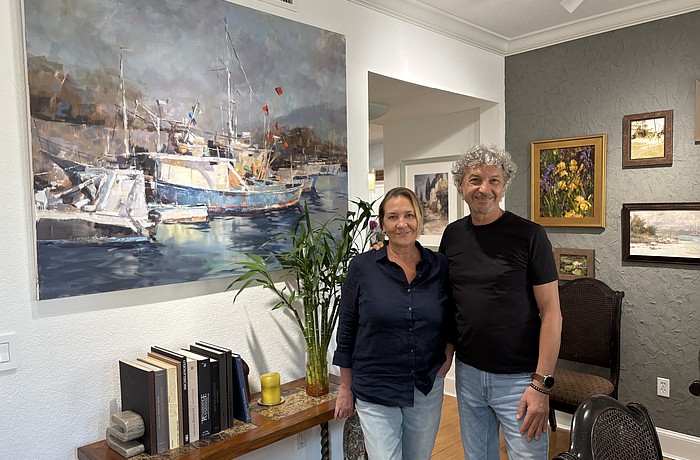 Marina and Vladislav Yeliseyev pose in front of one of Vlad's paintings in their home in The Landings.