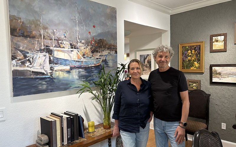 Marina and Vladislav Yeliseyev pose in front of one of Vlad's paintings in their home in The Landings.