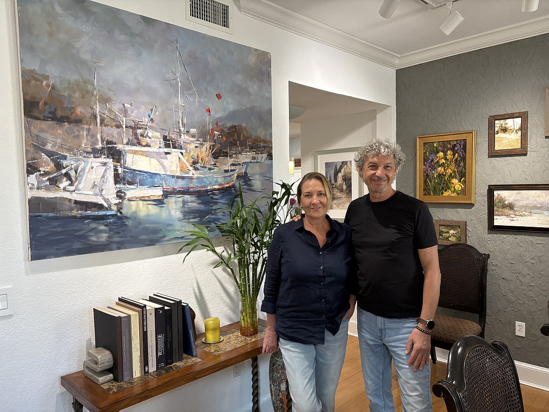 Marina and Vladislav Yeliseyev pose in front of one of Vlad's paintings in their home in The Landings.