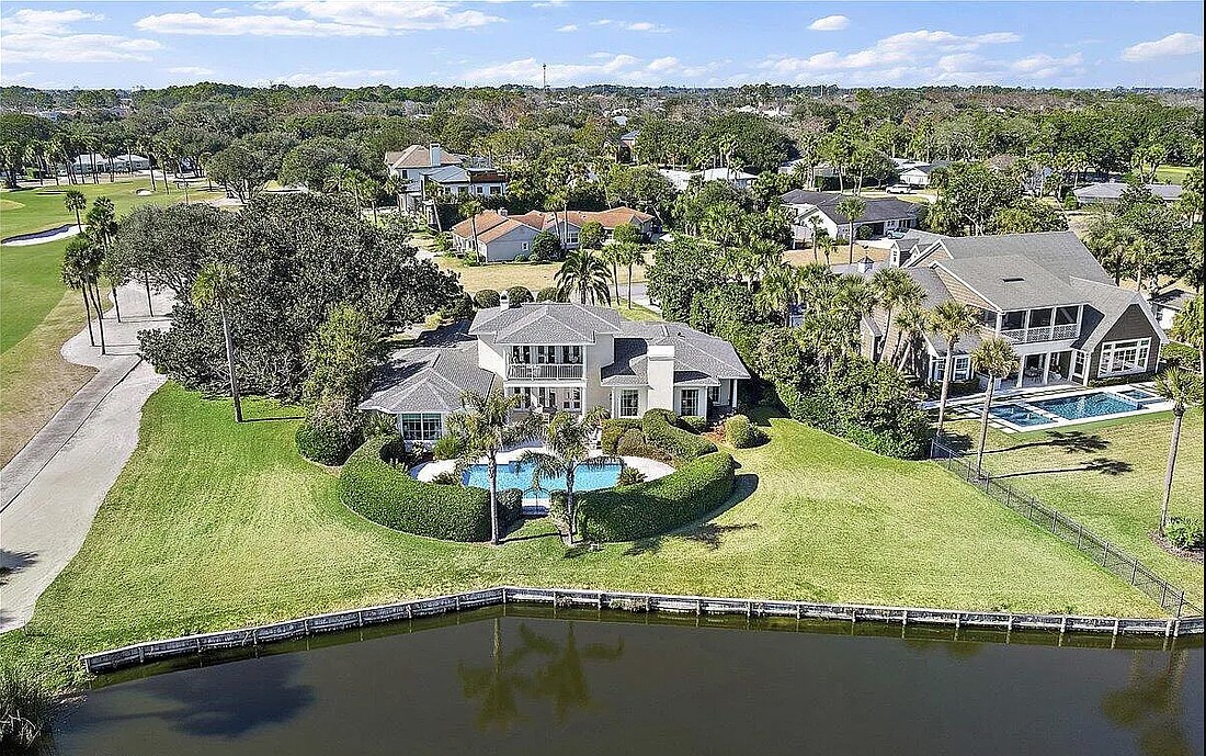 A waterfront two-story home with golf views featuring four bedrooms, three full and one half-bathrooms, an office, porches, a patio and swimming pool.