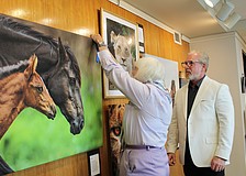 Photographer Rick Waid looks on as curator Anita Pihl affixes a blue ribbon to his piece, "Wild Mare with Foal," at the May 12 reception for a gallery by local photographers up now at Plymouth Harbor.