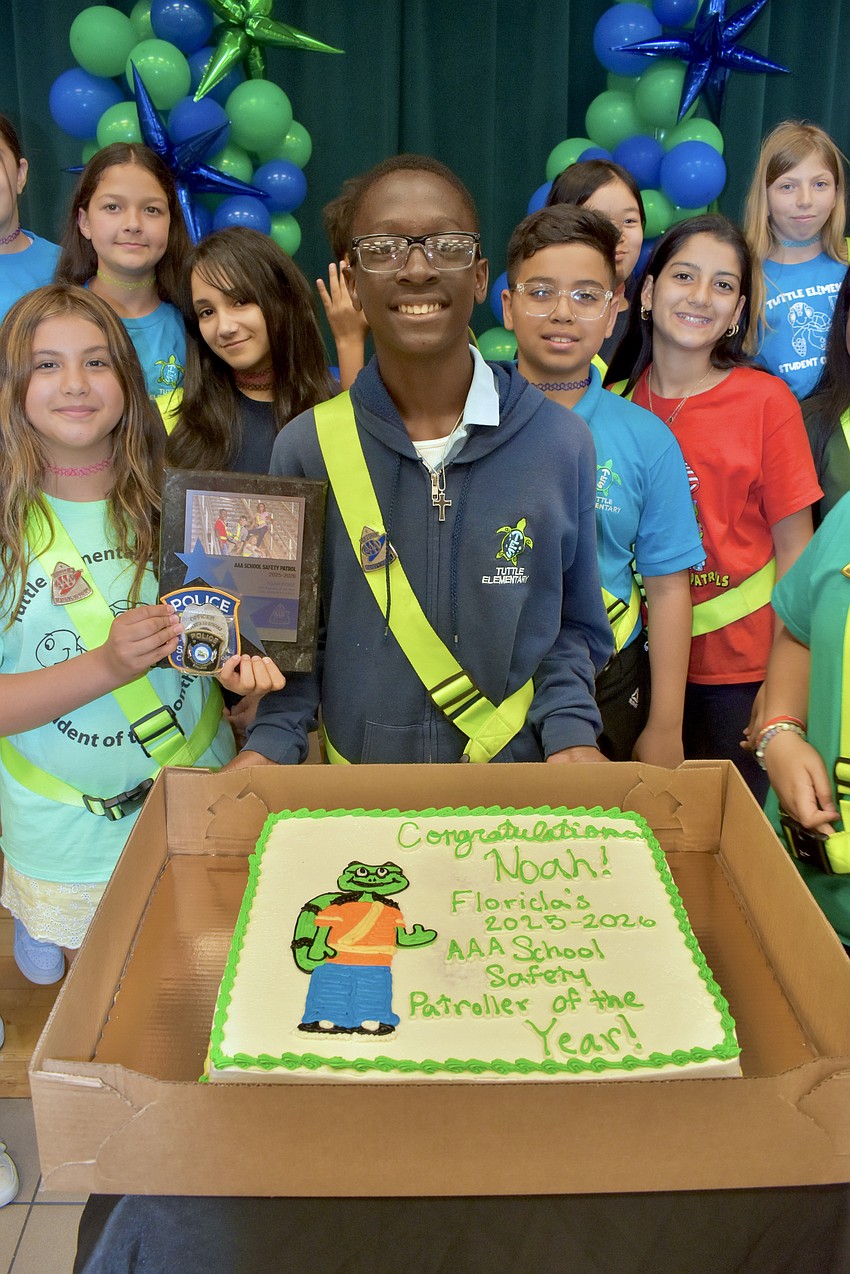Noah Moise and other students in the AAA School Safety Patrol program stand behind a cake made for him.