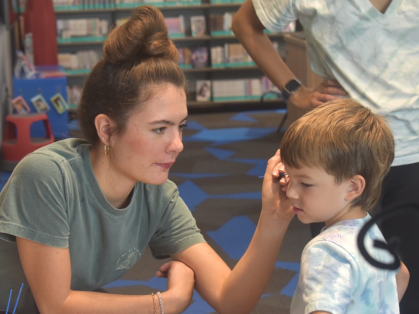 Lakewood Ranch's Kyla Logan, a member of the teen advisory board at the library, paints the face of 3-year-old Aiden Quijano during the Summer Learning Program Kickoff Party at the Lakewood Ranch Library.