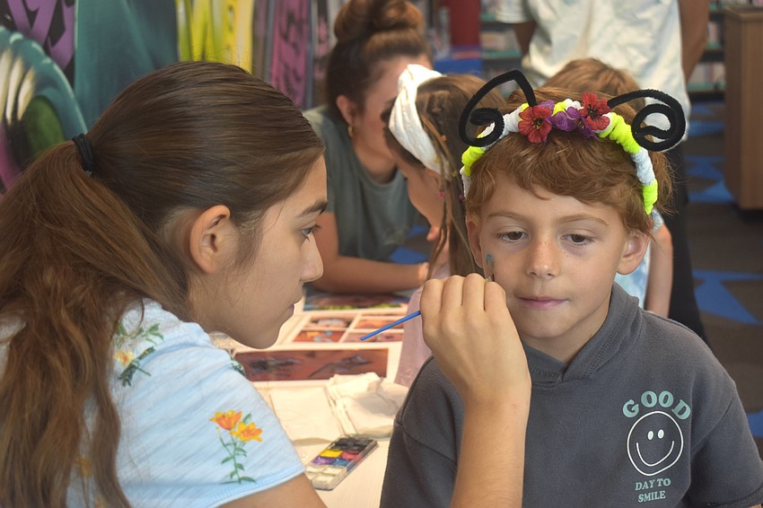 Isabella Hansen, a member of the teen advisory board at the Lakewood Ranch Library, paints two butterflies on the face of 6-year-old Lucas Weakley at the Summer Learning Program Kickoff Party.
