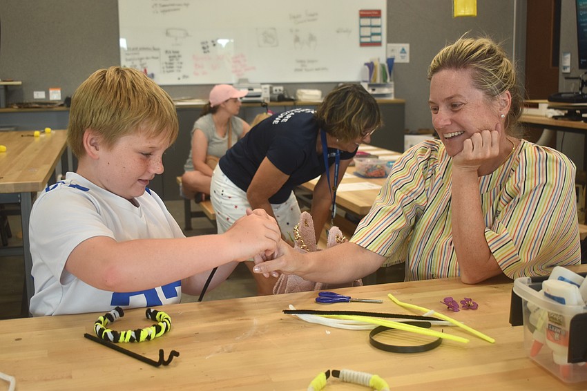 In order to twist the pipe cleaners into antennae for his headband, Reed Robson wraps it around the finger of his mom, Morgana Robson.