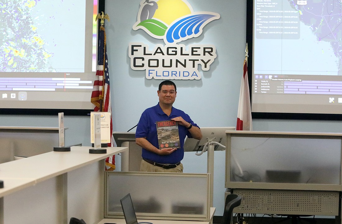 Flagler County Emergency Management Director Jonathan Lord poses inside the Emergency Operations Center's operations room. Lord is holding a copy of the Flagler County Emergency Preparedness Guide. Photo by Brent Woronoff