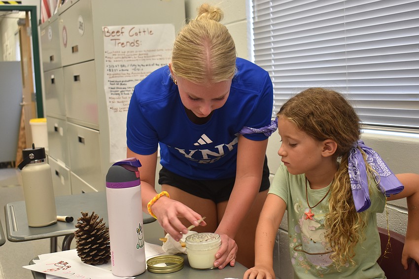 Gigi Canali, a member of FFA and camp counselor of 3 years, checks on the butter for 7-year-old Genevieve Shatraw.