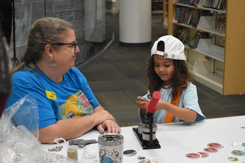 Children's success librarian Jenny Duckworth helps Uma Morilla, 5, create a button.