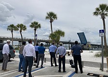 A drone flies over the Longboat Pass Bridge at an 80-foot elevation to contextualize what a fixed-span bridge would look live over the pass. Looking on (from left to right) are Longboat Key Commissioner Steve Branham, FDOT Southwest Area Office Director Wayne Gaither, FDOT Professional Engineer Trainee Stephen Pack, FDOT Project Manager David Turley, FDOT Project Development Manager Jimmy Vilce, FDOT Interim District One Secretary Jamie Driggers, Longboat Key Town Manager Howard Tipton and Longboat Key IT Director Jason Keen.