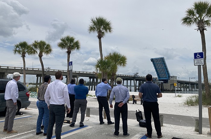 A drone flies over the Longboat Pass Bridge at an 80-foot elevation to contextualize what a fixed-span bridge would look like over the pass. Looking on (from left to right) are Longboat Key Commissioner Steve Branham, FDOT Southwest Area Office Director Wayne Gaither, FDOT Professional Engineer Trainee Stephen Pack, FDOT Project Manager David Turley, FDOT Project Development Manager Jimmy Vilce, FDOT Interim District One Secretary Jamie Driggers, Longboat Key Town Manager Howard Tipton and Longboat Key IT Director Jason Keen.