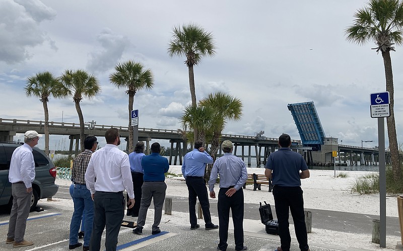 A drone flies over the Longboat Pass Bridge at an 80-foot elevation to contextualize what a fixed-span bridge would look like over the pass. Looking on (from left to right) are Longboat Key Commissioner Steve Branham, FDOT Southwest Area Office Director Wayne Gaither, FDOT Professional Engineer Trainee Stephen Pack, FDOT Project Manager David Turley, FDOT Project Development Manager Jimmy Vilce, FDOT Interim District One Secretary Jamie Driggers, Longboat Key Town Manager Howard Tipton and Longboat Key IT Director Jason Keen.