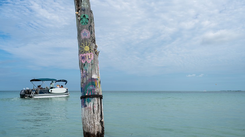 A driftwood trunk that stands in the water has been painted with messages from visitors to Beer Can Island. A driftwood trunk that stands in the water has been painted with messages from visitors to Beer Can Island.