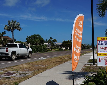 A feather banner is anchored next to the sidewalk on Gulf of Mexico Drive. Longboat Key staff are preparing an amendment that could prohibit that type of sign by refining the definition of flag in town code.