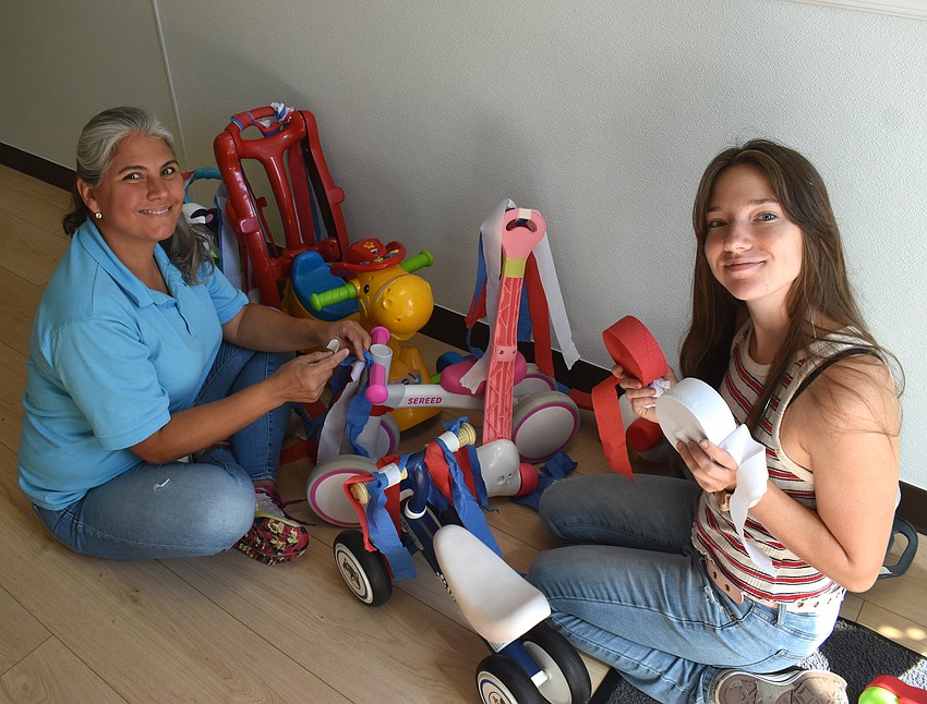 Kiddie Academy teachers Gladys Burbo and Savannah Dillahay decorate bikes for the children who are too young to do so themselves.