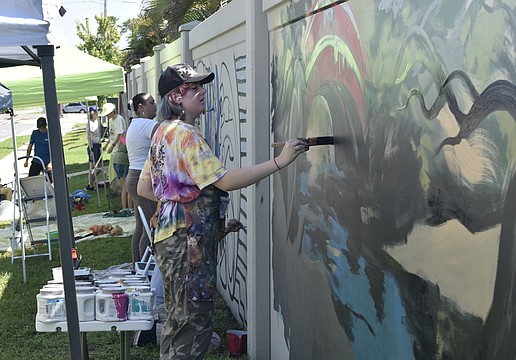 Ginger Kreithen works on "The Legacy," amid other artists at the wall.