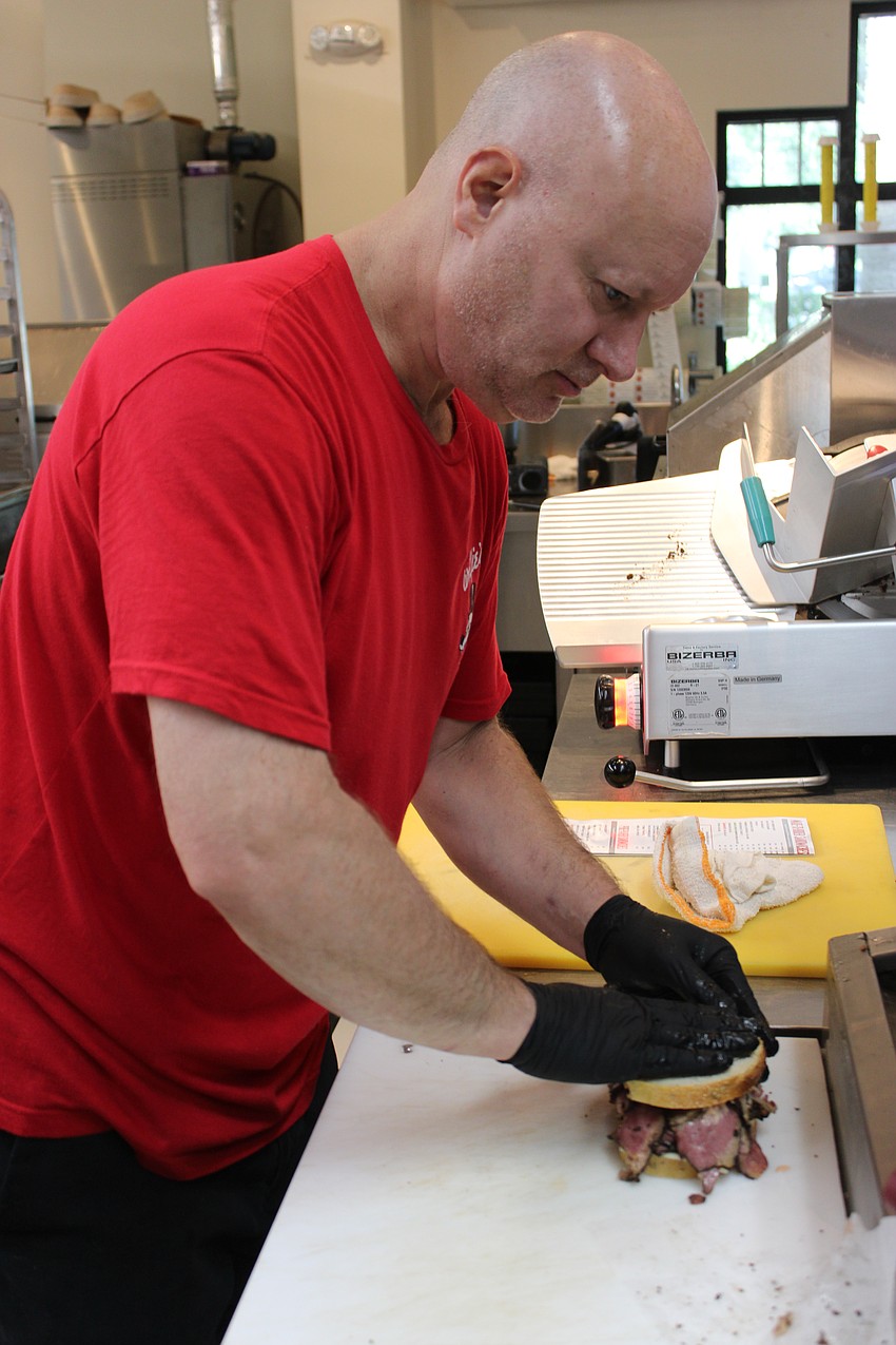 Original Wolfie's employee Tim McCann puts the finishing touches on a sandwich. McCann will be working at the Wolfie's Hand Cut when it opens late this year in UTC.