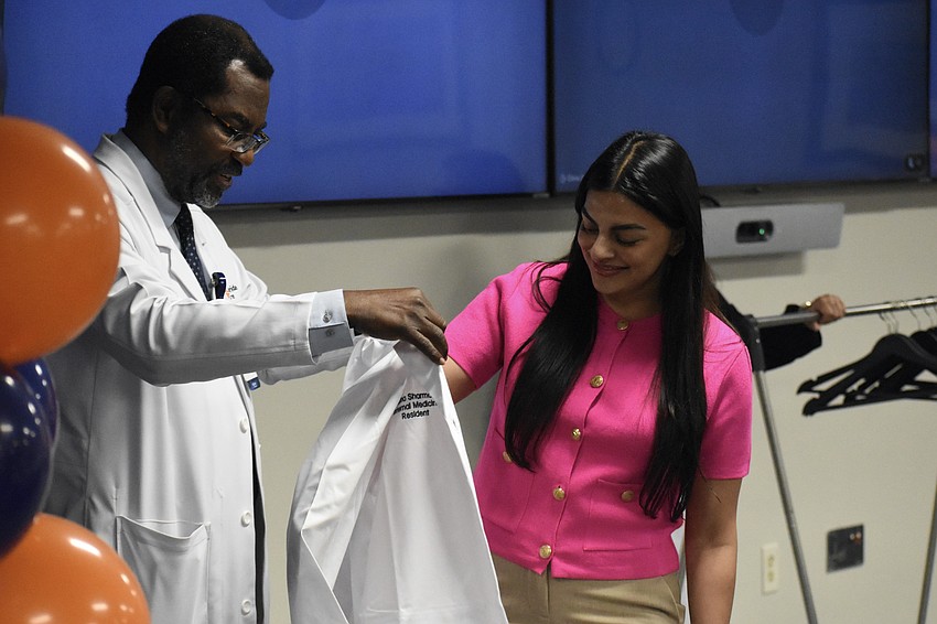 Dr. Michael Schandorf-Lartey, program director of internal medicine presents resident physician Dr. Natasha Sharma with a coat during a White Coat Ceremony for new physicians at HCA Florida Sarasota Doctors Hospital.